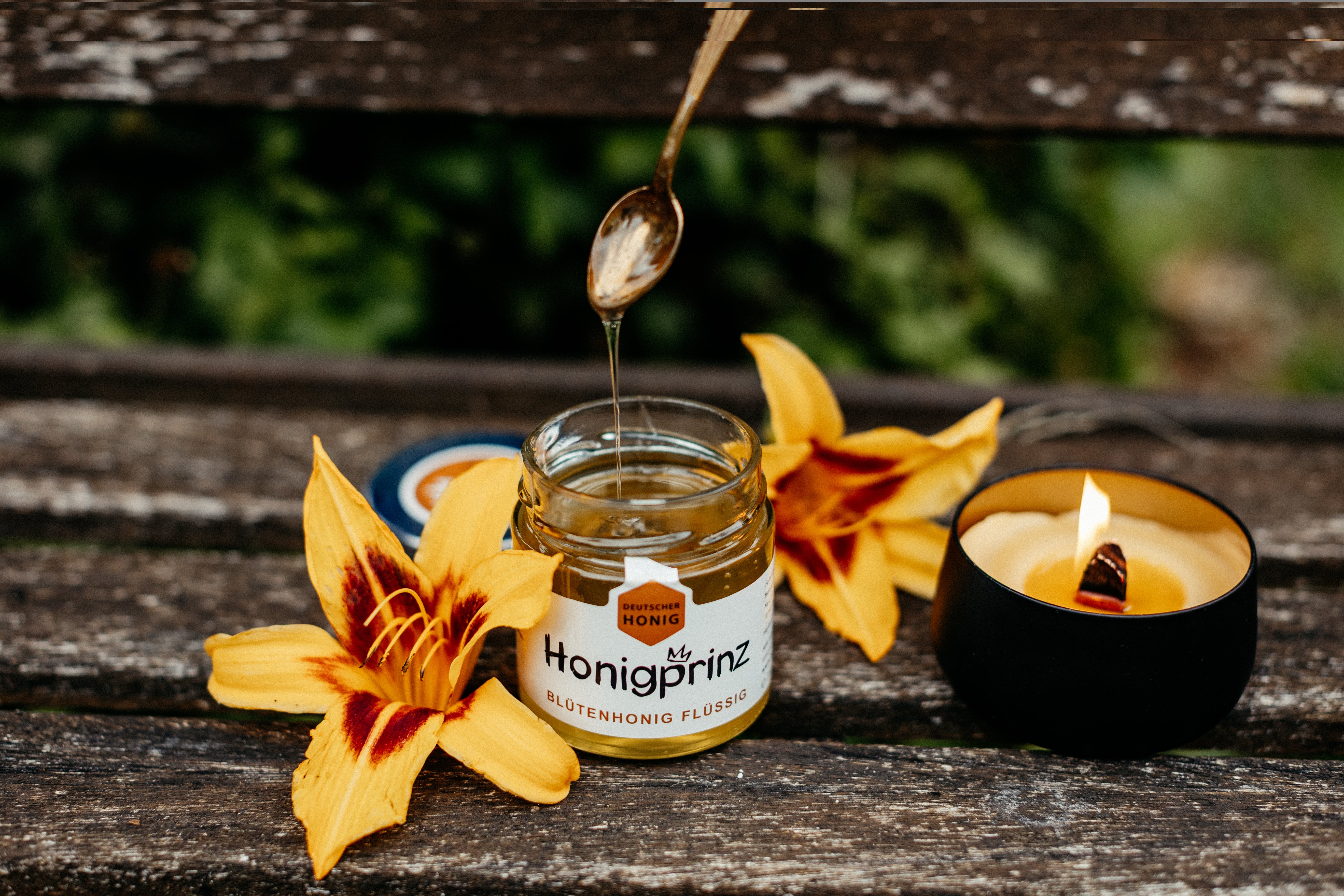 Löffel mit Honig von Honigprinz arrangiert zwischen gelben Blumen mit Knisterkerze