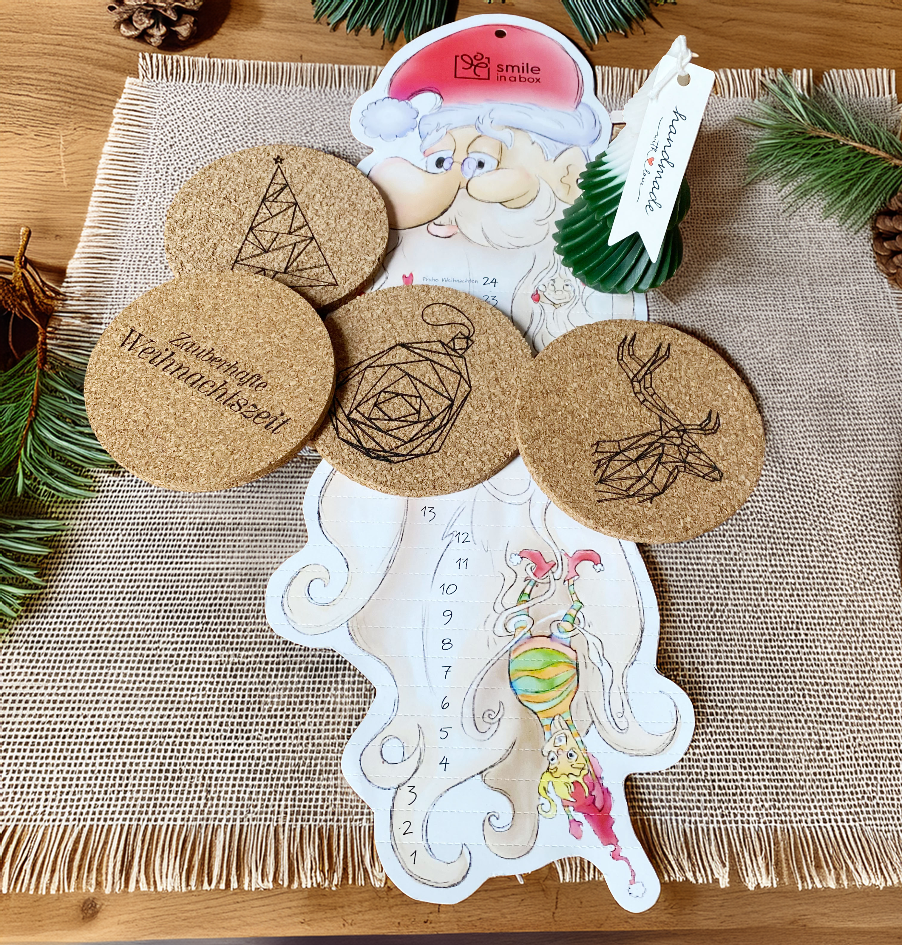 Kleine Weihnachtsgeschenkbox mit Kerze, Lebkuchen, festlichen Korkuntersetzern und Adventskalender auf festlich gedecktem Tisch - ideal als Kunden- oder Mitarbeitergeschenk