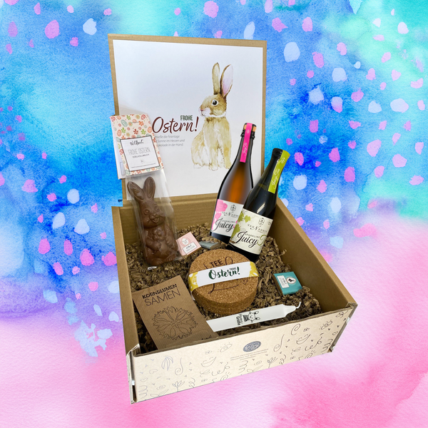 Osterüberraschung für Kunden mit Osterkerze, Schokohase, Schokotäfelchen, Juicy Tee, frühlingshaften Korkuntersetzern und Blumensamen arrangiert in Gecshenkbox. Auch ein perfektes Ostergeschenk für Mitarbeiter!