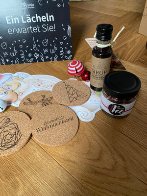 Größere Aufnahme der Weihnachtsgeschenkbox im Weihnachtsmarkt-Stil mit Tee, Mandeln, Sirup, Korkuntersetzern, Weihnachtskalender – ideal als Kundengeschenk
